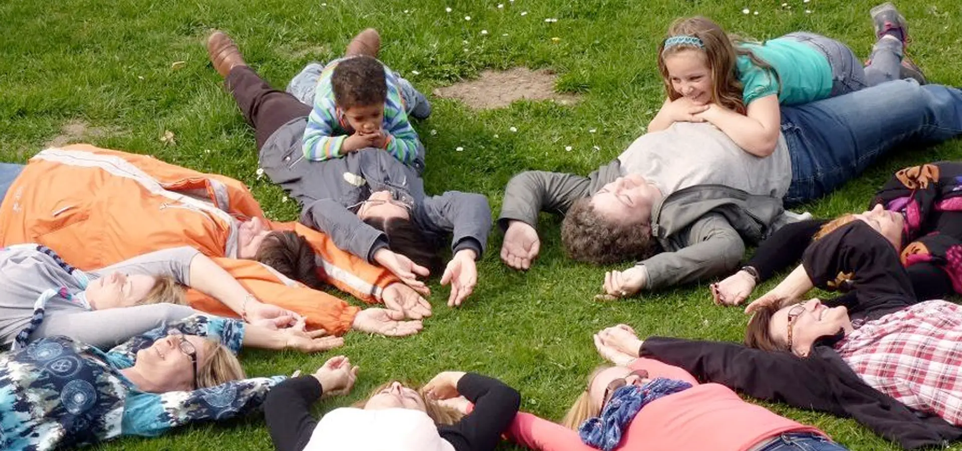 Gruppe von Menschen liegt im Kreis auf einer Wiese.