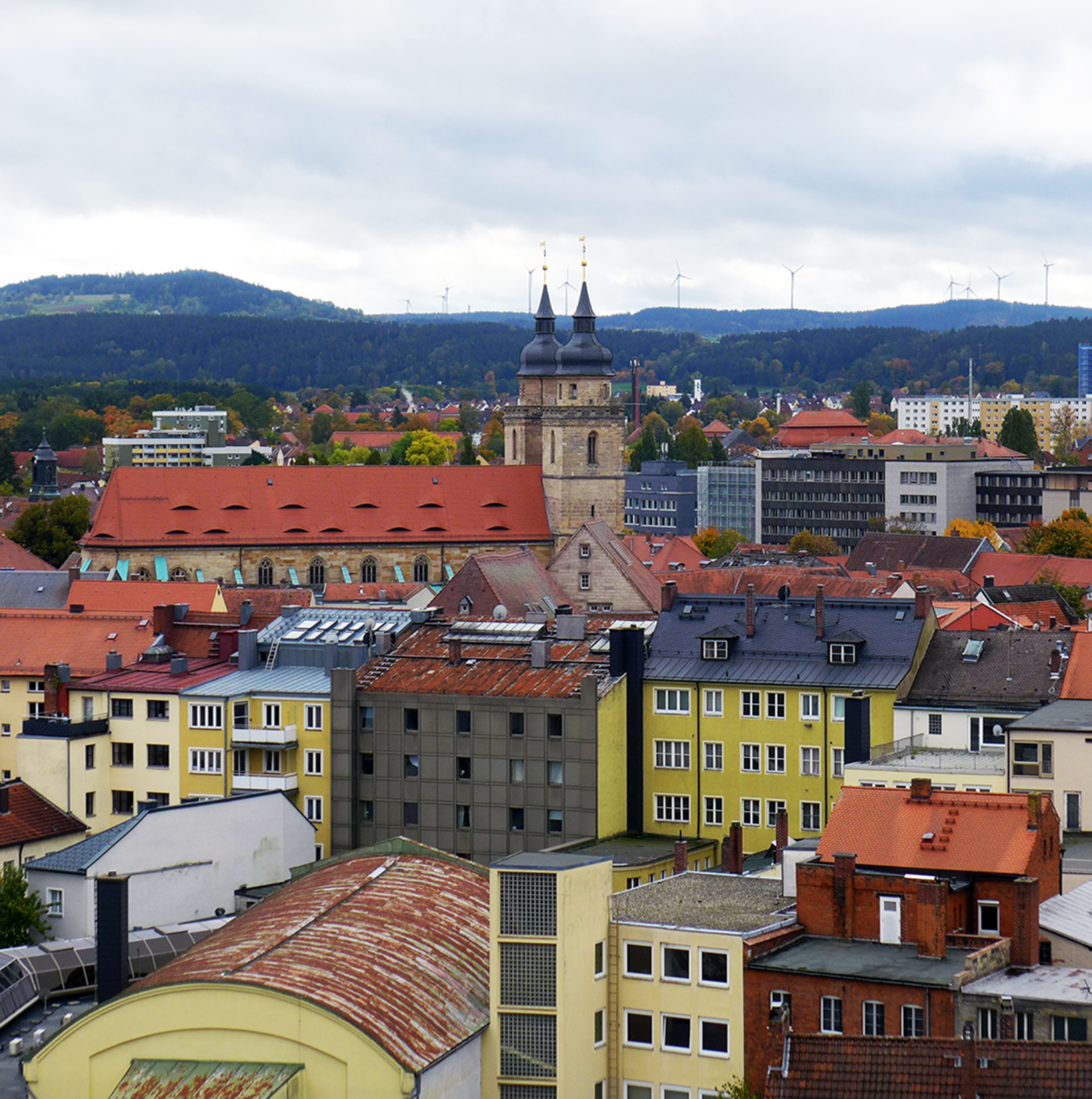 Stadtblick mit Kirche und bewaldeten Hügeln im Hintergrund.