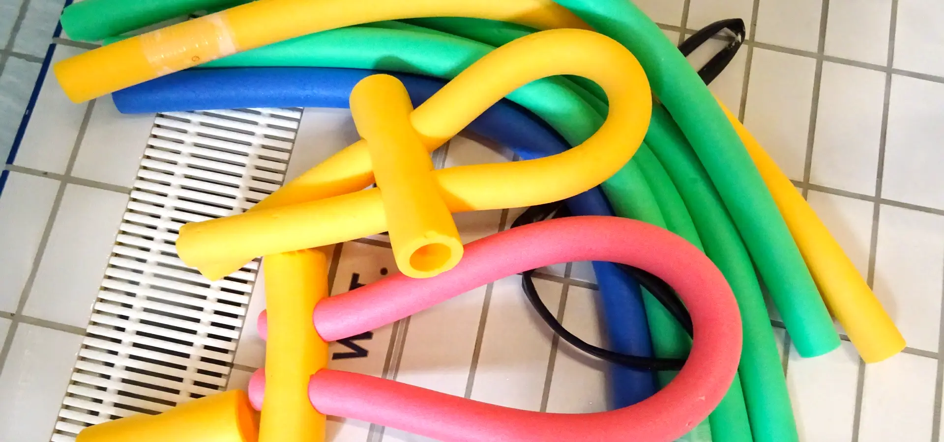 Bunte Schwimmnudeln auf Fliesenboden.