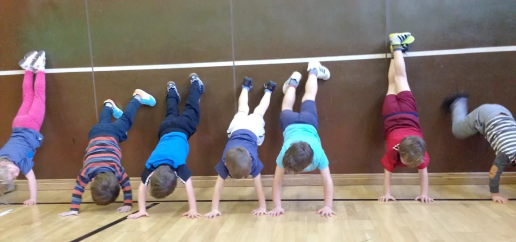 Kinder machen Handstand gegen eine Wand in einer Turnhalle