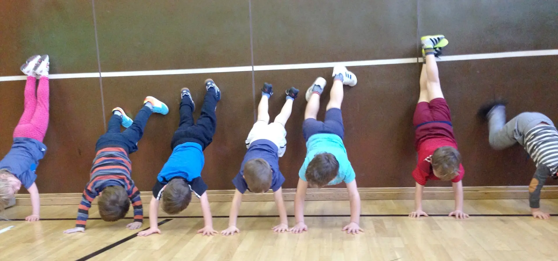 Kinder machen Handstand gegen eine Wand in einer Turnhalle