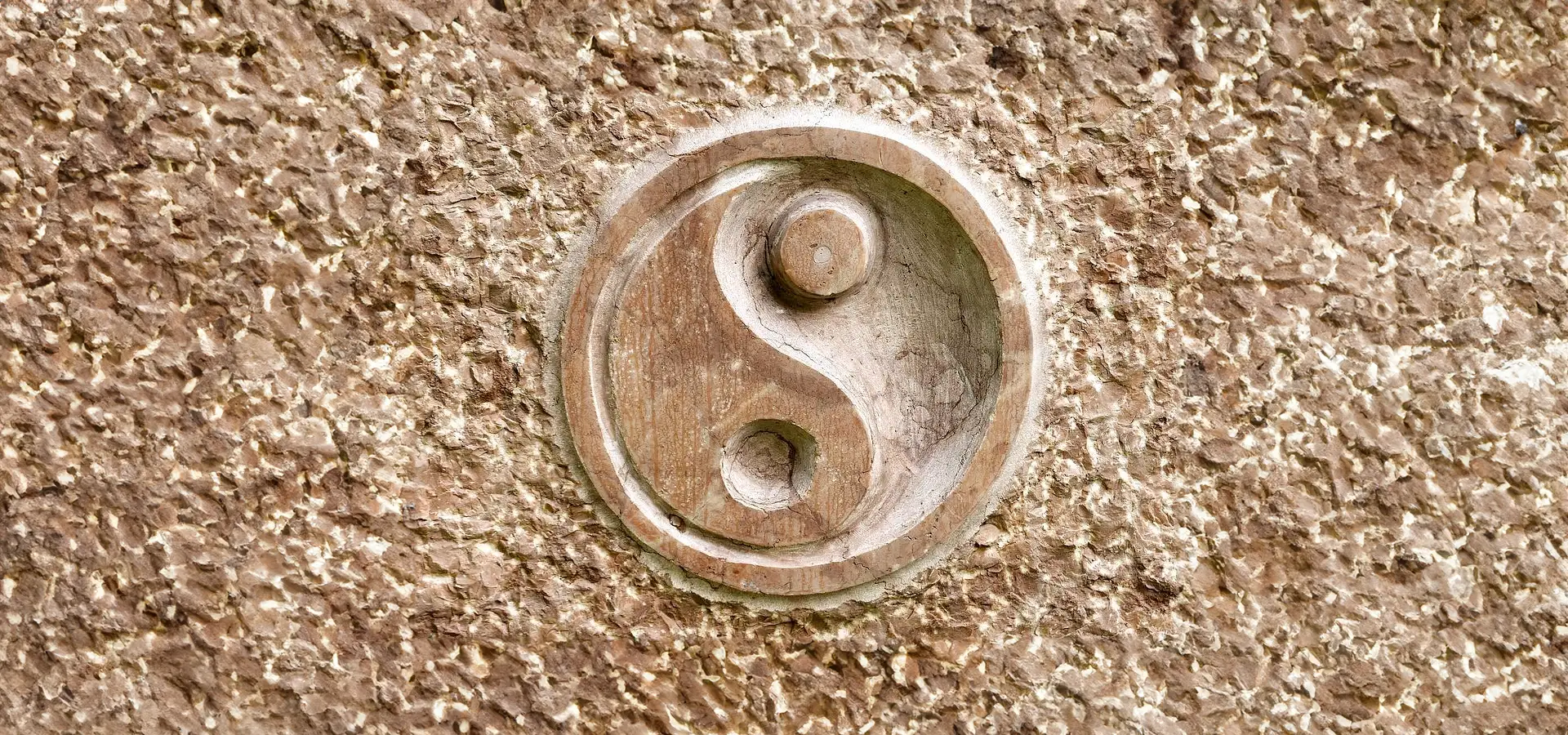 Holzschnitzerei von Yin-Yang-Symbol auf Steinwand.