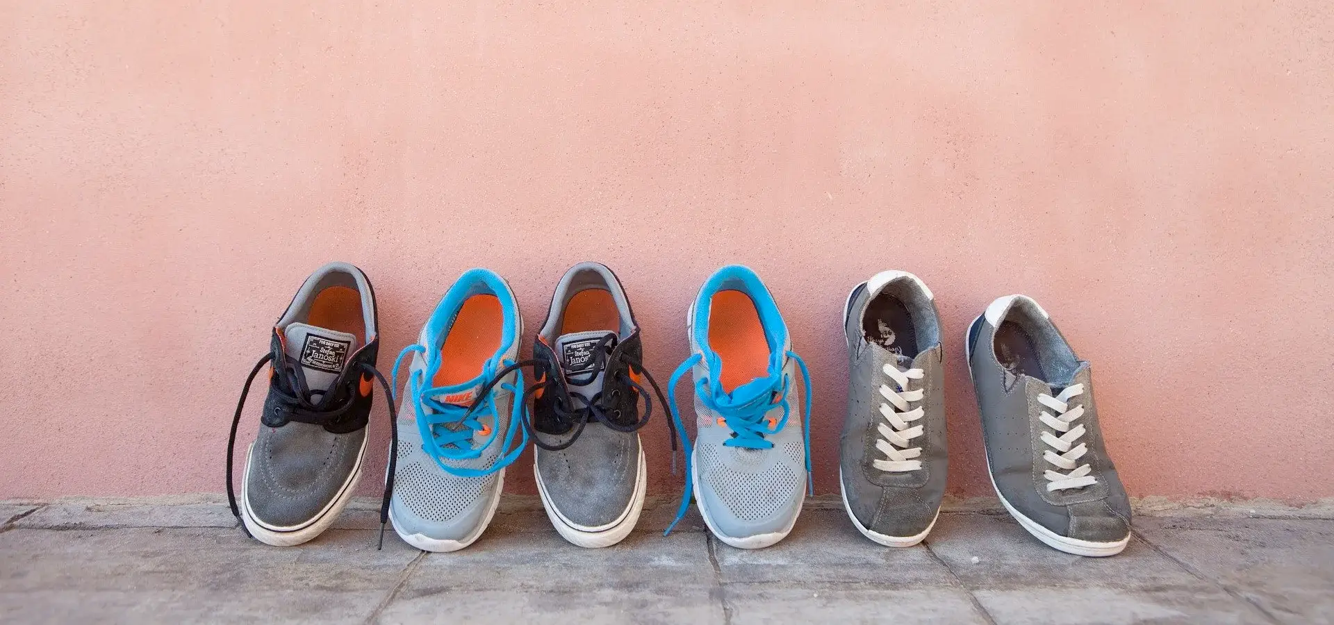 Vier Paar Sneakers in einer Reihe vor einer rosa Wand.