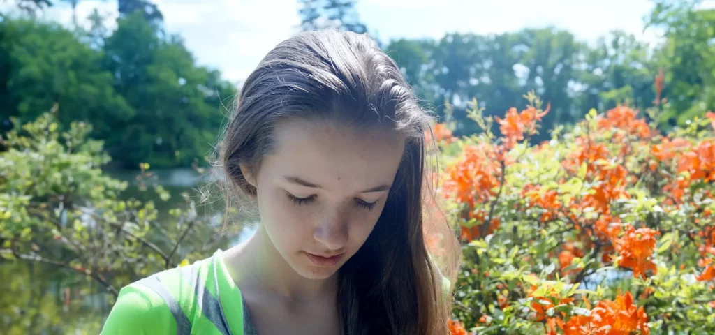 Mädchen mit gesenktem Blick vor Blumen.