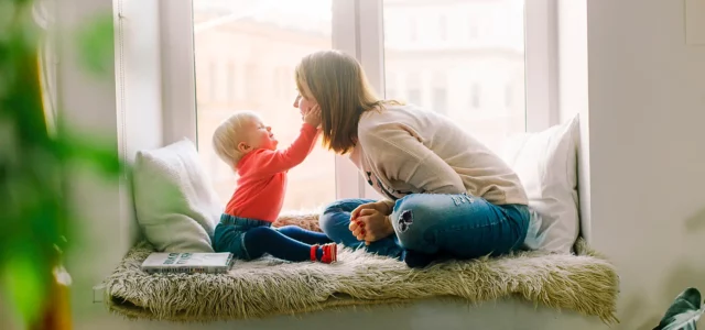 Mutter und Kleinkind spielen zusammen auf einem Fenstersitz