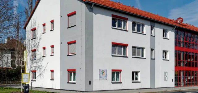 Weißes Gebäude mit roten Fensterrahmen und teilweise roter Fassade, Hausnummer