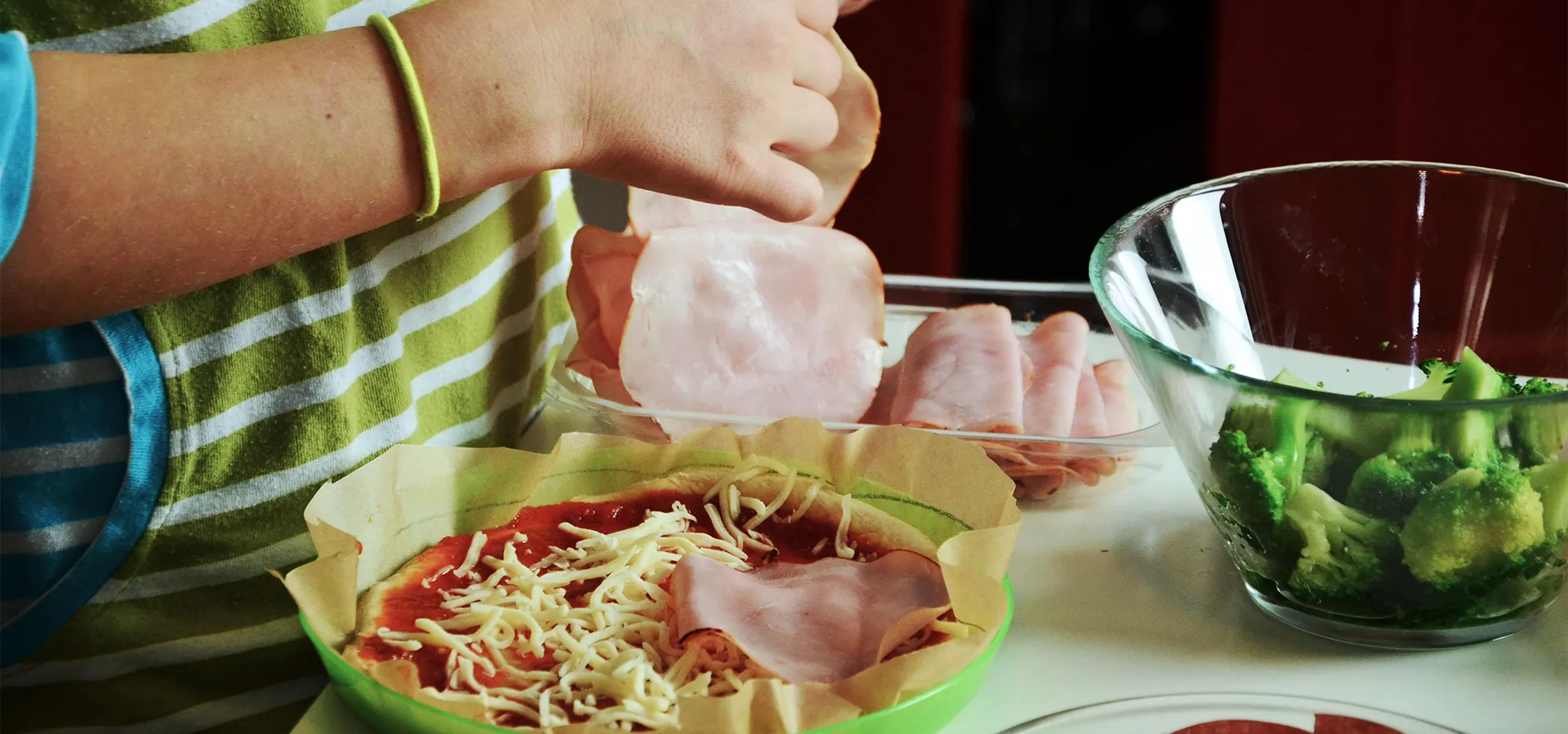 Kind bereitet Essen mit Schinken und Käse zu.