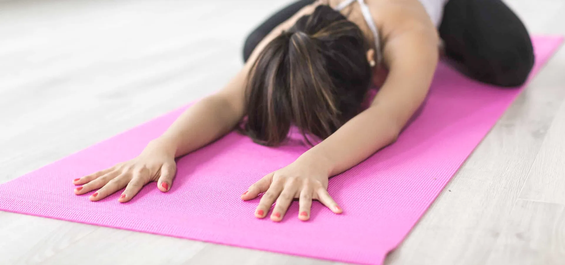 Person macht eine Yoga-Dehnübung auf einer rosa Matte.
