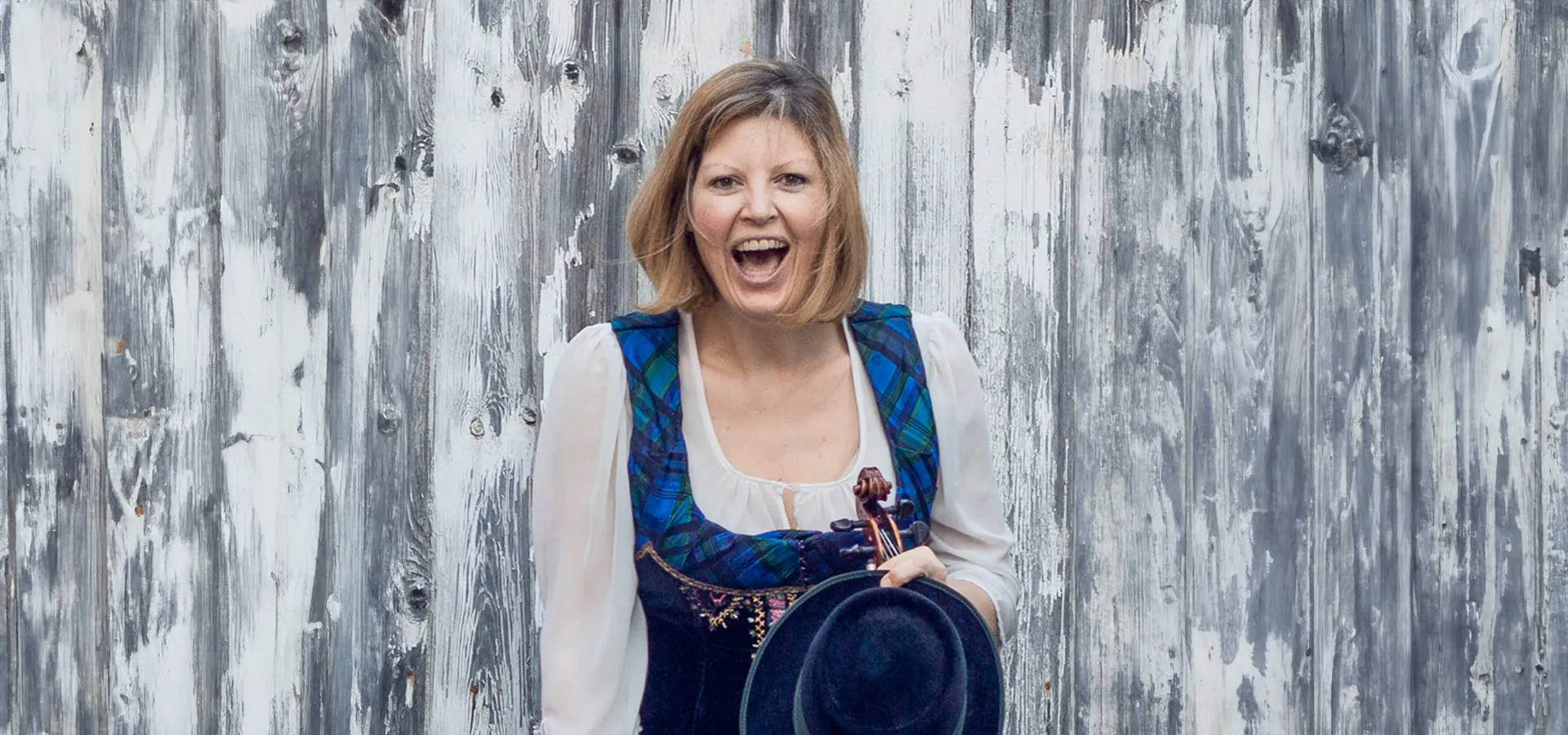 Frau in Tracht lacht vor Holzwand
