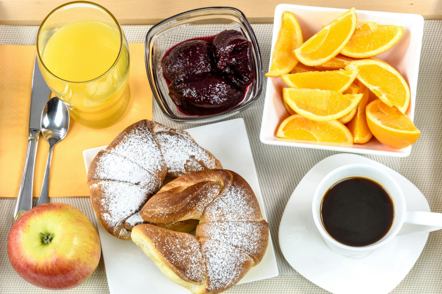 Ein Frühstück mit Apfel, Orangensaft, Marmelade, Orangen, Hörnchen und Kaffee