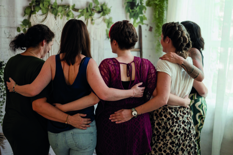 Frauen stehen Arm in Arm im Halbkreis mit dem Rücken zum Fotografen