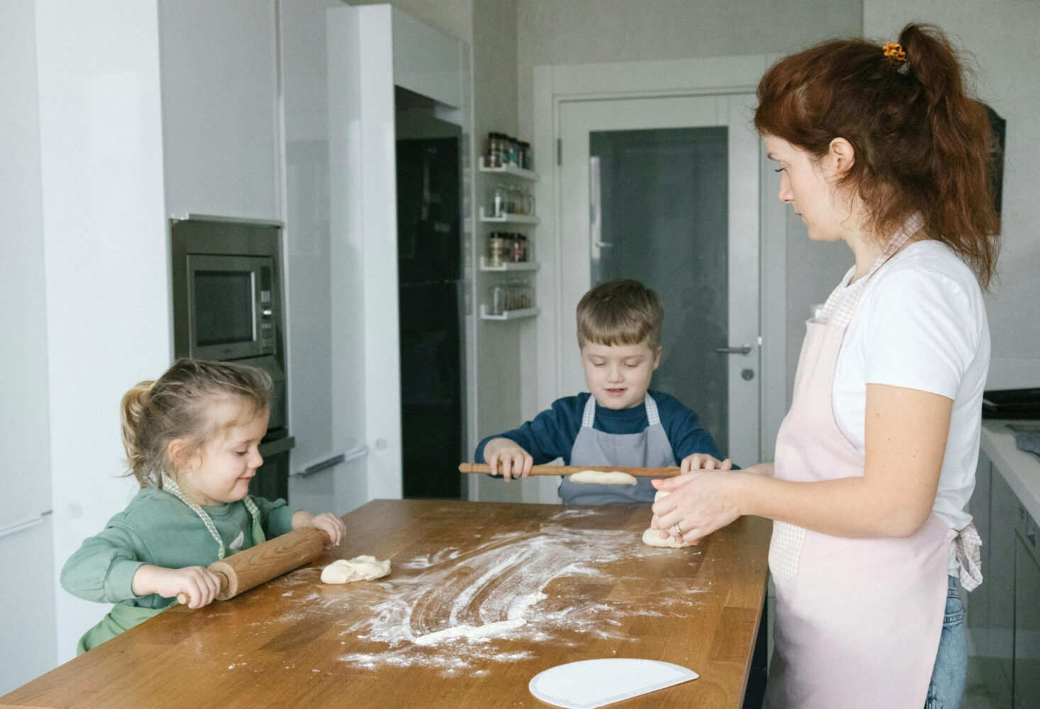 Eine Mutter knetet mit zwei Kindern Teig auf einem Küchentisch
