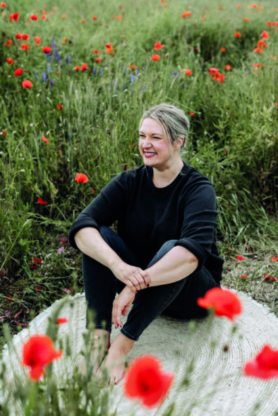 Daniela sitzt auf einem Teppich im Mohnfeld